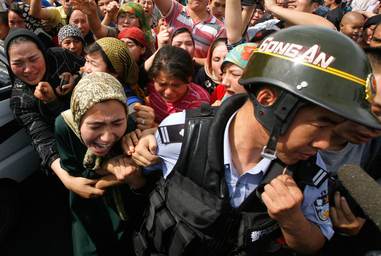 Image: A woman holds onto a Chinese policeman as a crowd of locals confront security forces along a street in the city of Urumqi