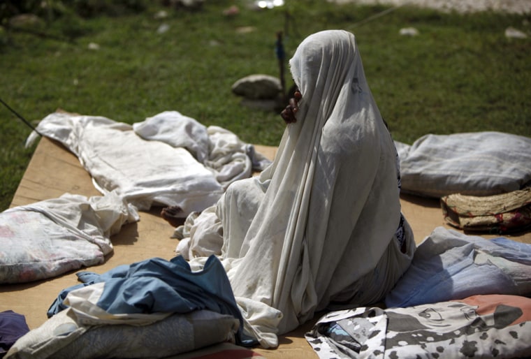 Image: A woman sits on a cardboard at a camp in Port-au-Prince