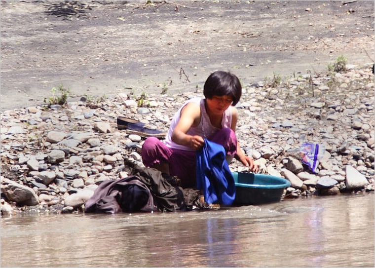 Image: Woman washes clothes in river.