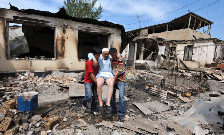 Image: People help an elderly ethnic Uzbek man in front of his burnt-out house