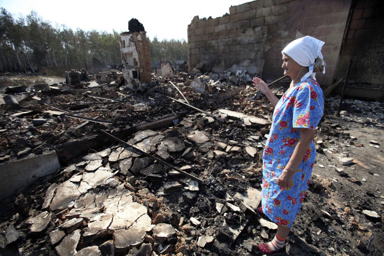 Image: A Russian woman looks at the remains of her burnt out home