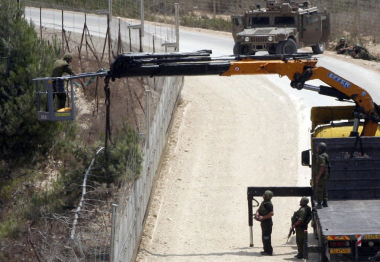 Image: Israeli soldiers use a crane as they appear to cut a tree on the Lebanese side of the border