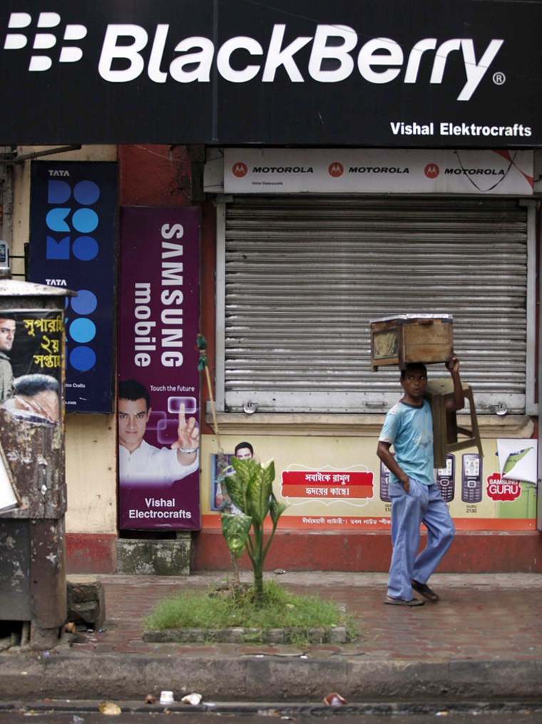 Image: A man with his belongings walks past a closed store selling mobile phones in Kolkata