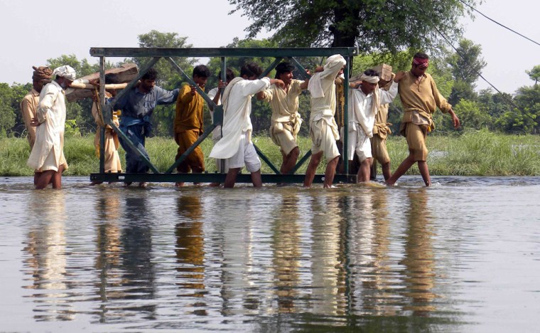 Image: Flood victims carry a portion of a bridge as they try to rebuild it