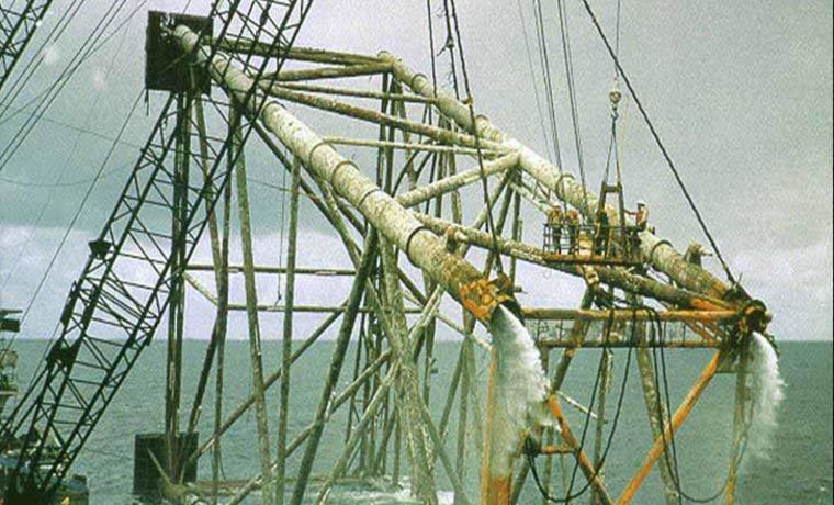 A platform "jacket" from a decomissioned well is lifted out of the water. The structures are often mammoth in size — notice the workers at right.