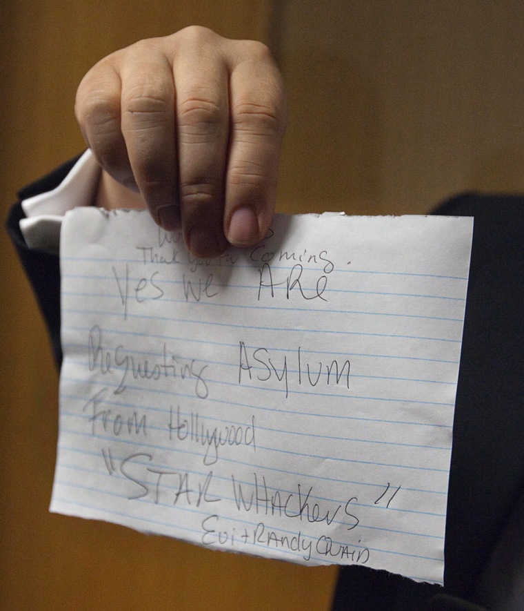 Image: Tsuji, lawyer for actor Randy Quaid and his wife Evi, holds up a note the couple wrote and read to media outside a Canadian Immigration and Refugee Board hearing in Vancouver