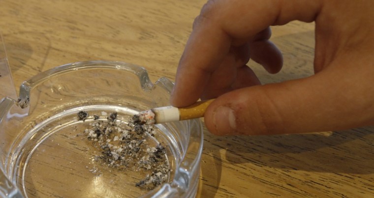 Image: A man holds a cigarette next to a smoking ban sign in a cafe in Chalandri suburb, north of Athens