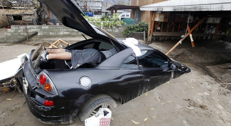 Image: John Regalado Jr. takes out personal items from his partially-submerged car after heavy rains and flooding brought mud and debris into his house