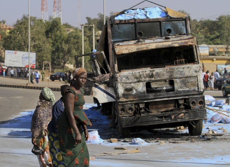 Image: People walk past the wreckage of a burnt truck along a road in Nigeria's central city of Jos