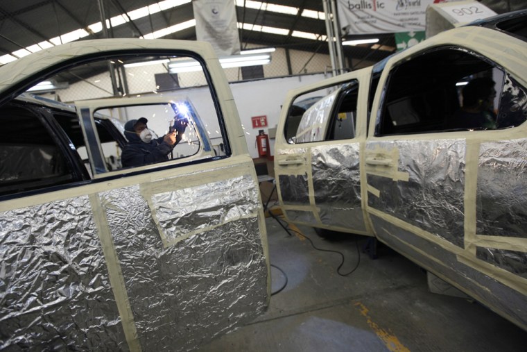 Image: A welder works on fitting bulletproof glass in the door of a car at a garage in Mexico City