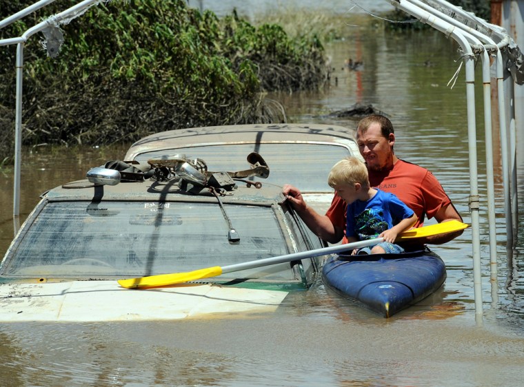 Image: Scott Wogandt and his son Mitchell kayak past flooded cars in Bundaberg on Dec. 31