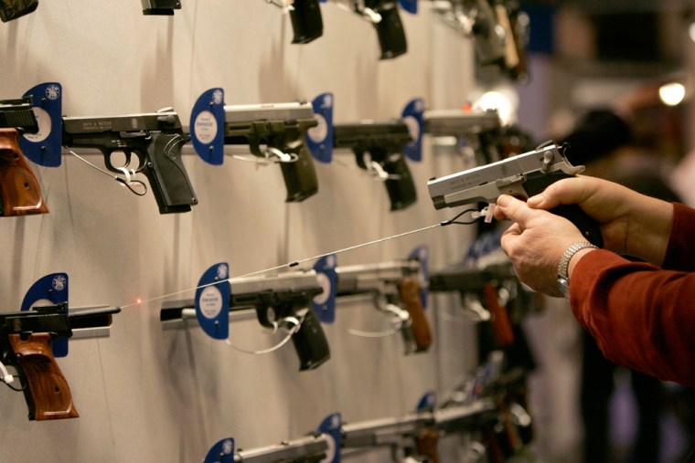 Image: A woman points a handgun with a laser sight on a wall display of other guns during the National Rifle Association convention