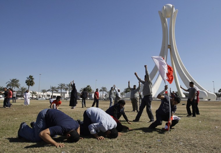 Image: Bahraini protesters pray and  chant slogans as another protester, right,  places a Bahraini flag at the Pearl roundabout