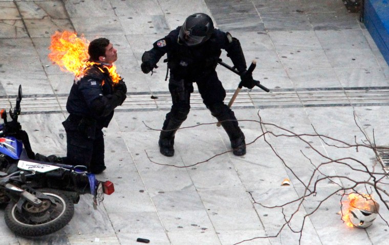 Image: A motorcycle policeman burns as his colleague tries to help him after protesters threw a petrol bomb in Athens