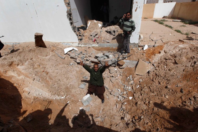 Image: An anti-Gadhafi rebel gives V sign as he stands in a crater at a house that attacked by an air strike by pro-Gadhafi warplanes, in the town of Ras Lanouf, eastern Libya,