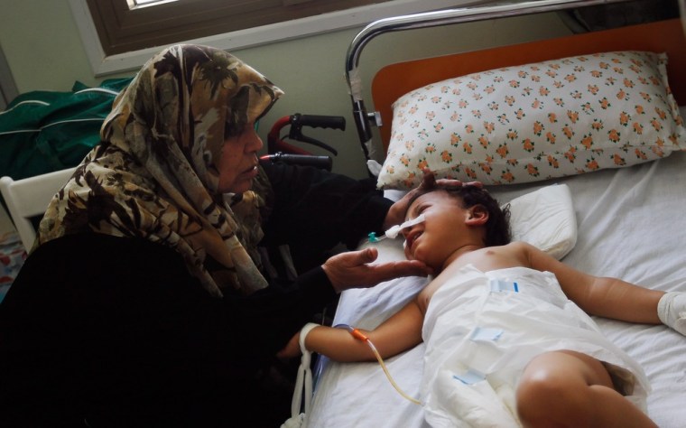 Image: Selima Abdullah (L) caresses her youngest granddaughter Heba, who suffered a ripped-open abdomen from shrapnel, after an explosive shell landing near her home during fighting in the besieged city of Misrata