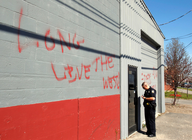 Image: Police officer stands next to graffiti-covered building
