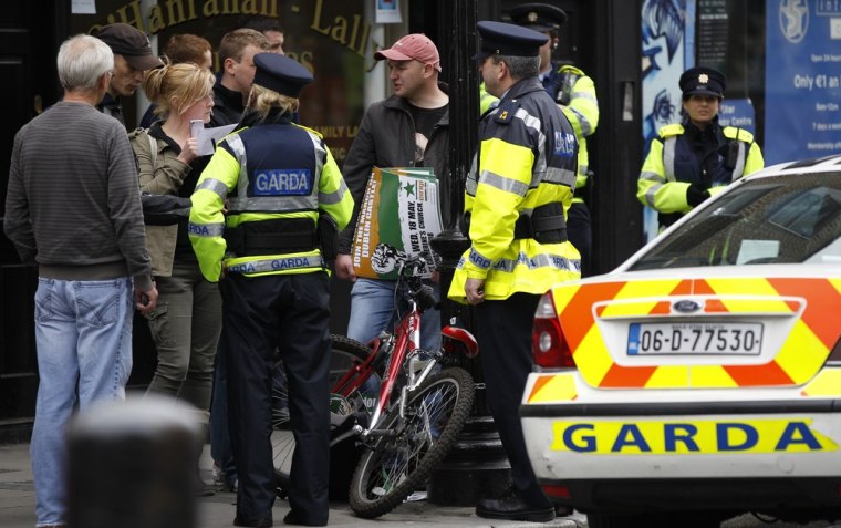 Image: Members of the Irish Police force question a group of people with anti - royal visit posters in Dublin