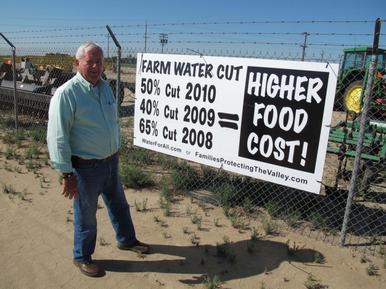 Image: Joe Marchini of Marchini Farms stands in front a water cutbacks sign on the flanks of his field