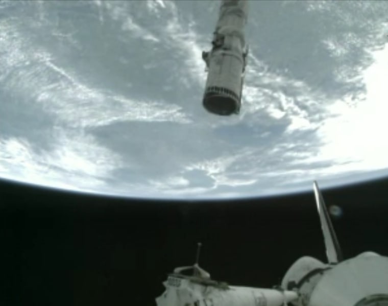 A video frame from NASA TV shows the view of Earth from orbit, with the shuttle Atlantis' tail sticking up from the bottom of the frame and its robotic arm sticking down from the top.