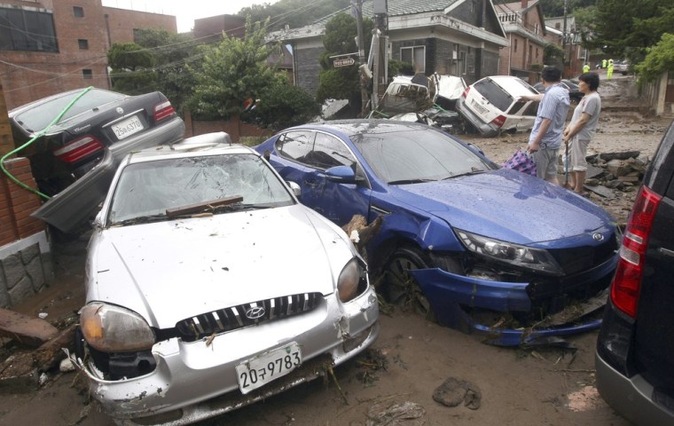 Image: Residents look at a village as they stand beside wrecked vehicles after a heavy rainfall in Seoul