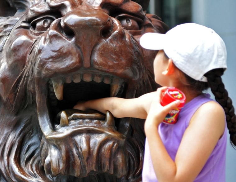Image: A young girl places her arm inside a lion statue outside the HSBC headquarters in Hong Kong