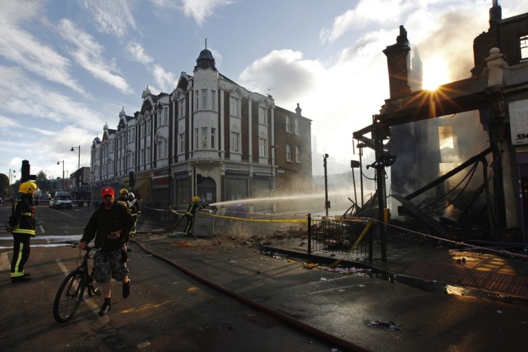 Image: A cyclist passes firefighters near buildings set alight during riots in Tottenham, north London