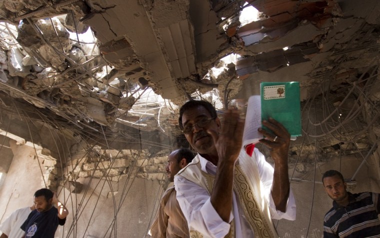 Image: A man shows children books found in home officials say was destroyed by NATO bombings in Majar