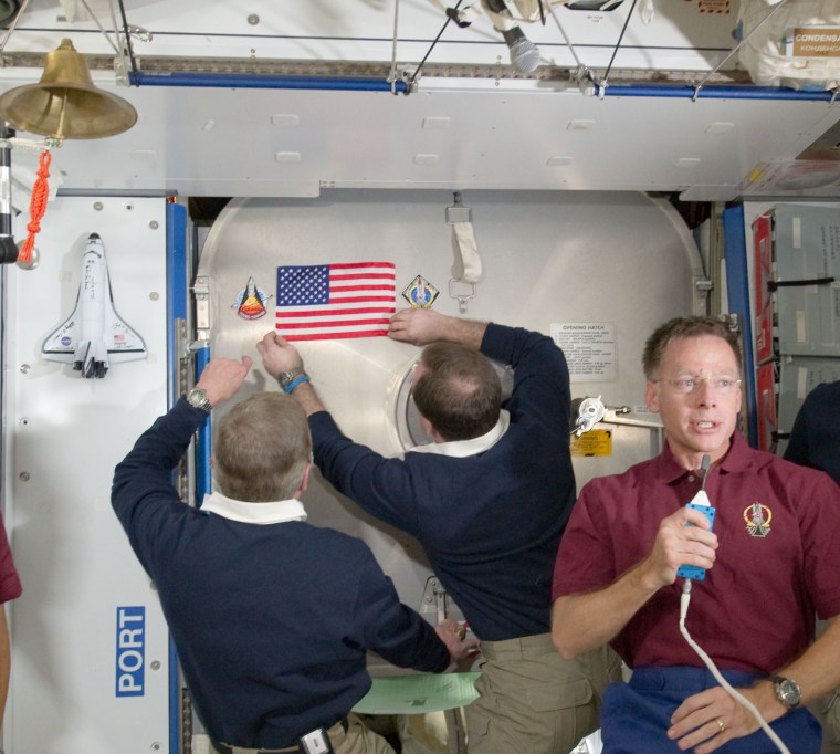 Symbolism abounds in this July 18 image from the International Space Station: Atlantis commander Chris Ferguson speaks to the camera during the last shuttle flight, while NASA space station crew members attach a US. flag to a hatch. The flag flew on the first space shuttle mission in 1981, and will be awarded to the next U.S. crew to be launched to the station from U.S. soil.