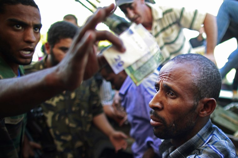 Image: A rebel fighter holds money and documents seized from a man they said is a Libyan army soldier in Zawiyah