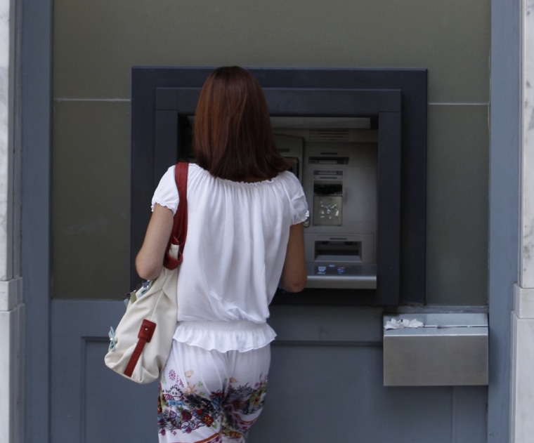 Image: A woman makes a transaction at an automated teller machine outside an Alpha bank branch in Athens