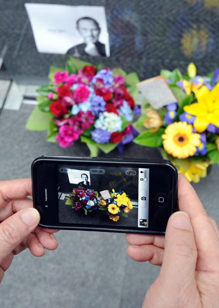 Image: A passerby uses an iPhone 4 to photograph flowers left for the late Steve Jobs in Sydney