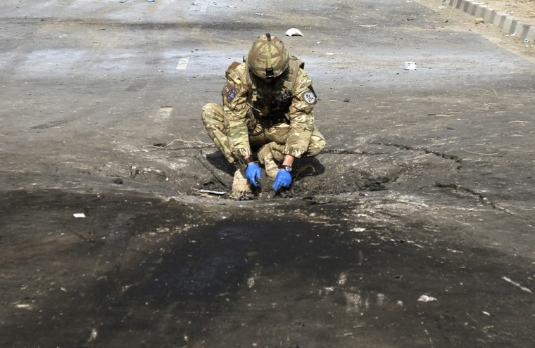 Image: A foreign soldier investigates the crater caused by an explosion at the site of a suicide attack in Kabul