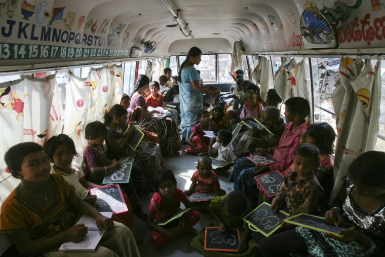 Image: Children write letters from the Telugu alphabet as a teacher conducts lessons inside a bus converted into a school called \"School on Wheels\", at a slum area in the southern Indian city of Hyderabad.