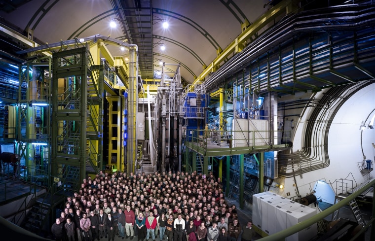 The LHCb team stands in front of their experiment, the LHCb detector, at the Large Hadron Collider in Geneva.