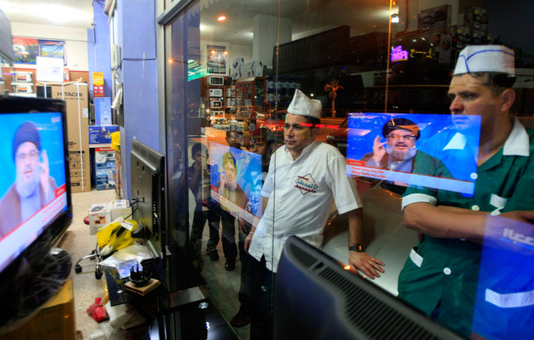 Workers at a nearby restaurant watch the televised speech of Hezbollah leader Hassan Nasrallah as they stand outside a shop in the southern port city of Sidon, Lebanon, on June 24.