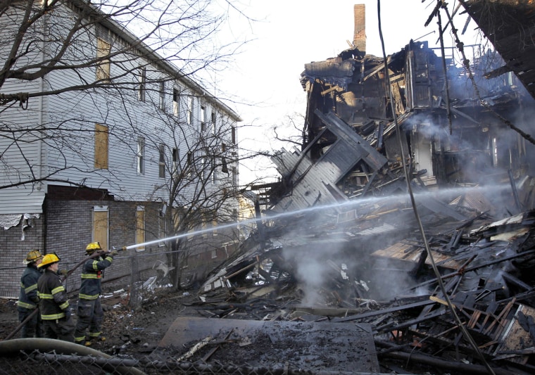 Image: irefighters spray water on the fire-damaged remains of a multi-family home