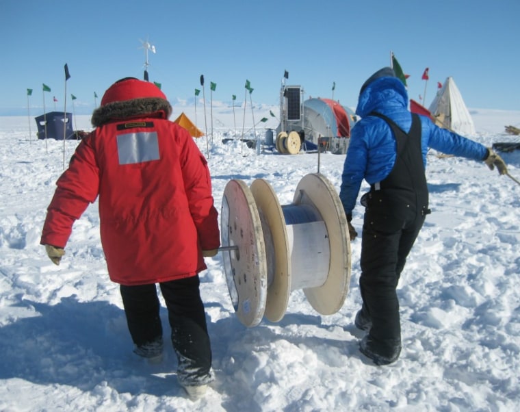 Scientists carry a spool of fiber-optic cable headed for duty inside and underneath the Ross Ice Shelf in Antarctica. 