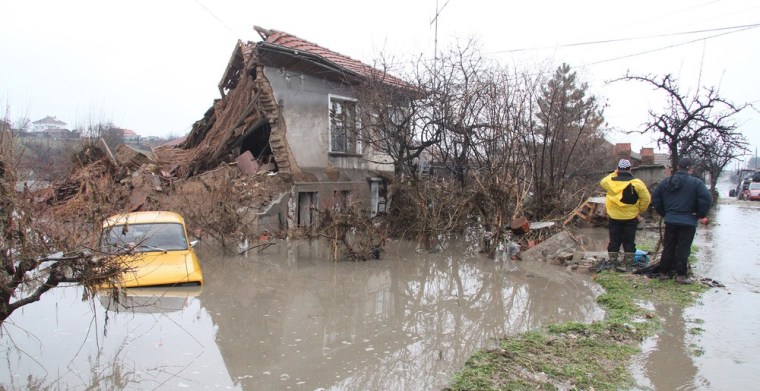 Image: People stand near a destroyed house in the village of Biser