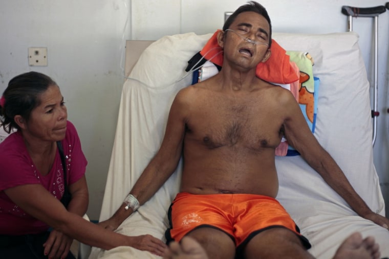 Image: Segundo Zapata Palacios rests in a hospital as his wife Emma Vanegas sits at his bedside
