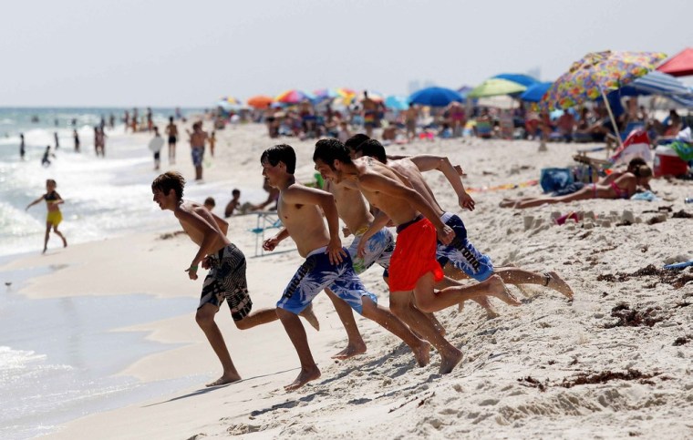 Image: Young men run into the waters of the Gulf of Mexico while playing on the beach in Perdido Key