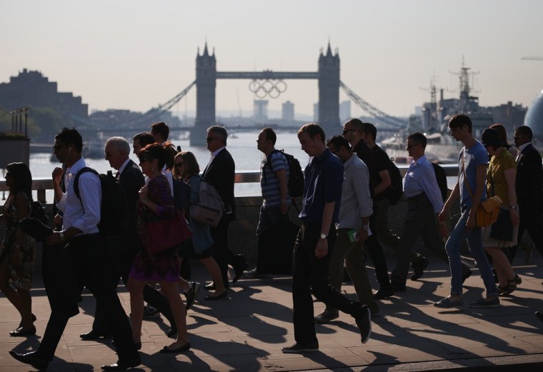 Image: Commuters walk across London Bridge as the Olympic Rings hang from Tower Bridge in the background