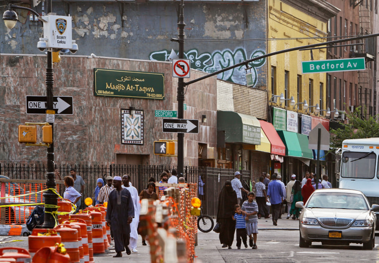 Image: people pass below a New York Police security camera, upper left, situated above a mosque on Fulton St., in the Brooklyn neighborhood of Bedford-Stuyvesant in New York
