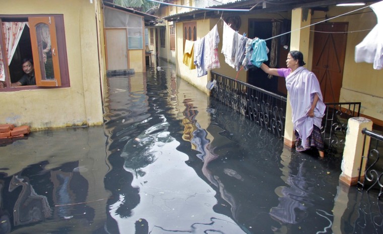 Image: A woman hangs her clothes outside her partially submerged home during flooding in Pandu