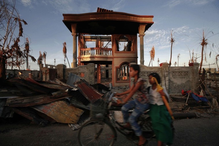 Image: Girls ride a moped past a burnt house during the violence at East Pikesake ward, in Kyaukphyu