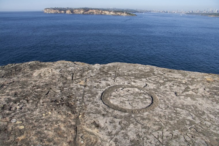 Inscriptions carved near the edge of a cliff with Sydney's skyline in the distance. Photo copyright Ursula Frederick