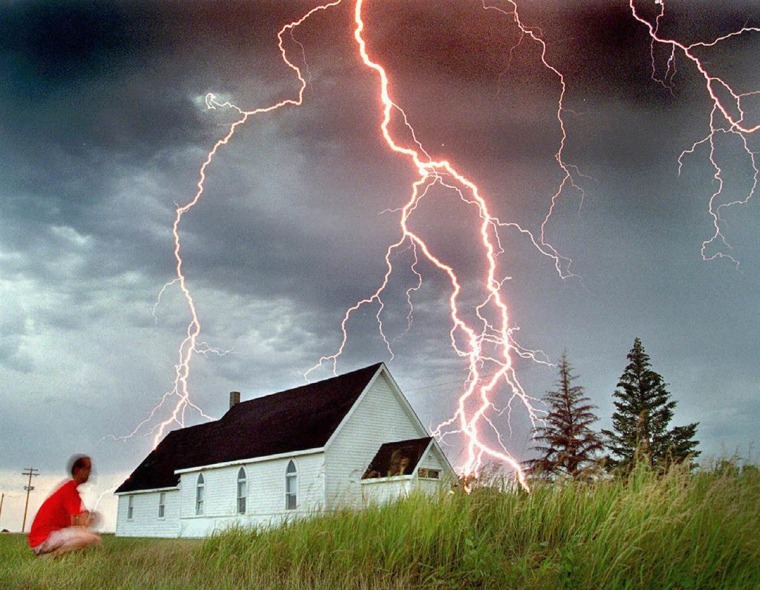 Neil Fraser watches as lightning hits beyond a church in Rosser, Manitoba, early in the morning on July 30, 1995.