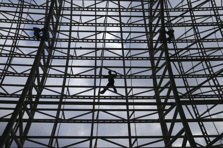 Image: A worker climbs the facade for construction of the Bolshoy ice dome, the hockey venue for the Sochi 2014 Winter Olympics, in Adler, near Sochi