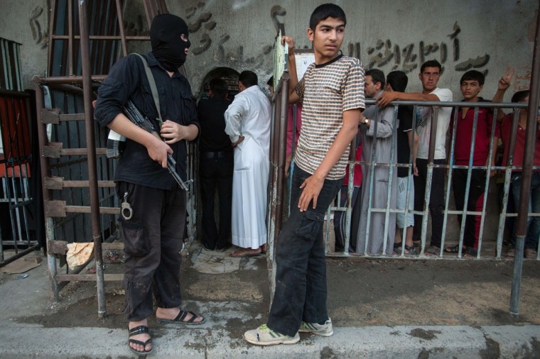 Image: An armed man wearing a balaclava stands guard outside a bakery run by the Islamic rebel group Ahrar Al-Sham