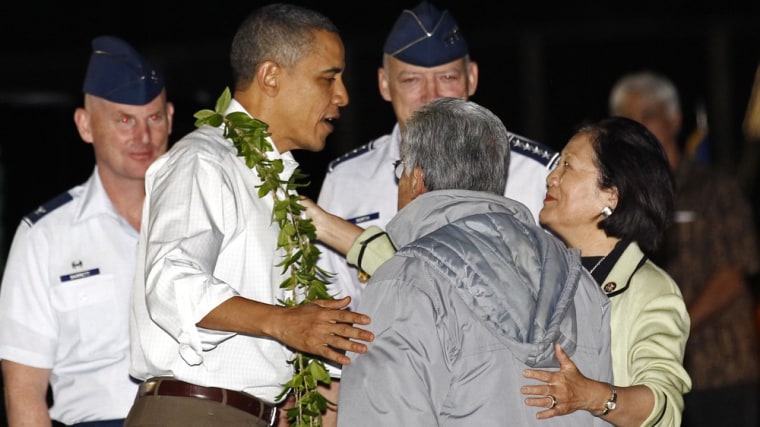 Image: U.S. President Obama has a lei around his neck as he talks with Senator Daniel Okaka and Rep. Mazie  Hirono upon his arrival  in Hawaii